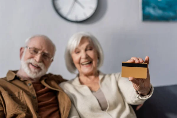 Selektiver Fokus einer glücklichen Seniorin, die neben lächelndem Ehemann ihre Kreditkarte zeigt — Stockfoto