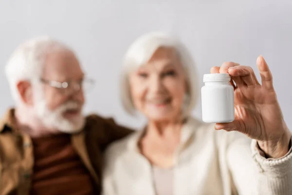 Selective focus of smiling senior woman showing pills container near cheerful man — Stock Photo