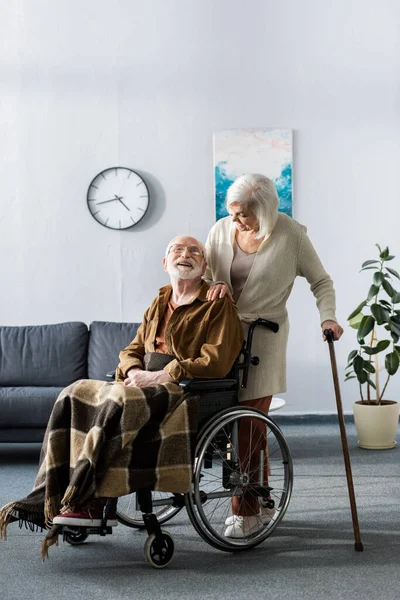 Mujer mayor con bastón y hombre discapacitado en silla de ruedas sonriendo mientras se miran - foto de stock