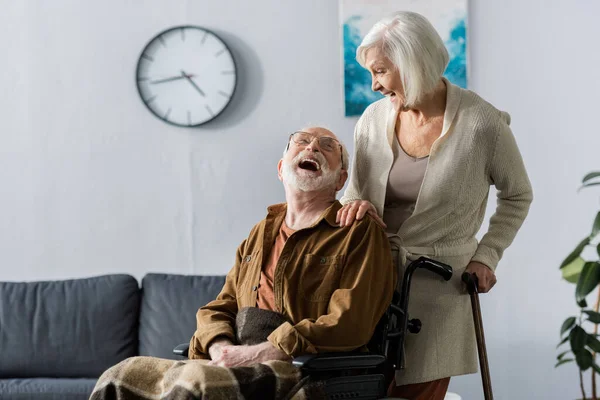 Senior wife and cheerful husband in wheelchair laughing while looking at each other — Stock Photo