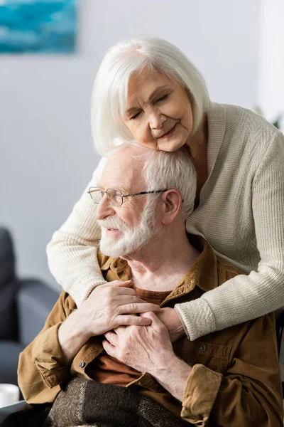 Mujer mayor con los ojos cerrados abrazando marido discapacitado — Stock Photo