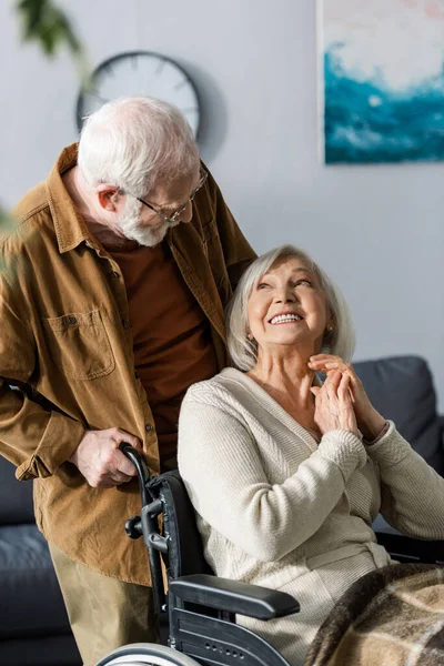 Старший чоловік дивиться на щасливу інвалідну дружину, сидячи в інвалідному візку — стокове фото
