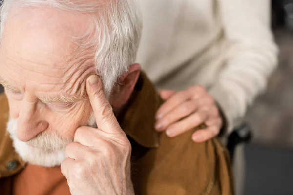 Cropped view of woman touching shoulder of husband, sick on dementia, sitting with closed eyes and touching head — Stock Photo