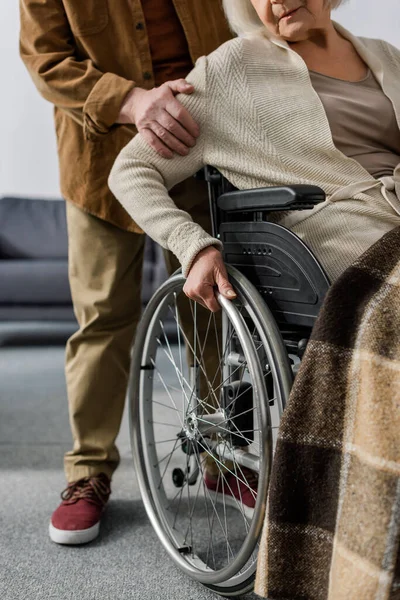 Cropped view of senior man touching arm of handicapped, diseased wife in wheelchair — Stock Photo