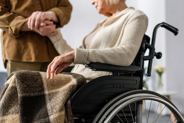 Cropped view of senior man holding hand of handicapped, ill wife in wheelchair — Stock Photo