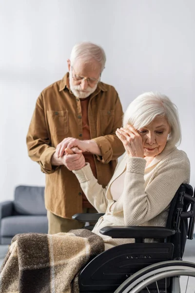 Senior man holding hand of handicapped, diseased wife crying in wheelchair — Stock Photo