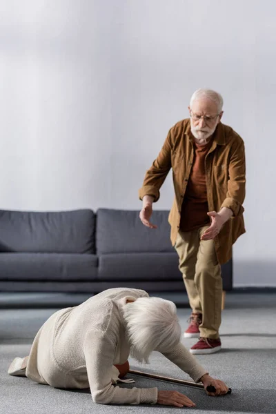 Uomo anziano che si affretta ad aiutare la moglie sdraiata sul pavimento vicino bastone da passeggio — Foto stock