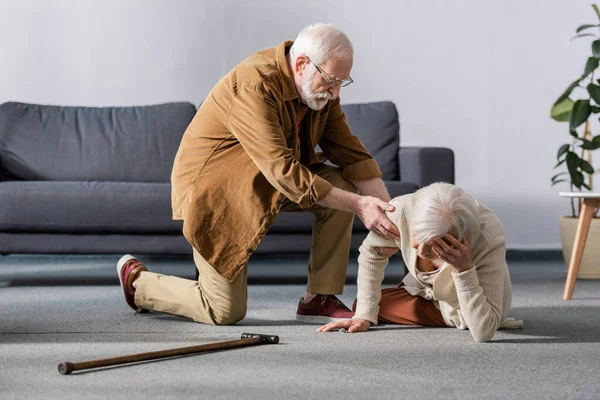 Uomo anziano aiutare moglie sdraiata sul pavimento e toccare la testa — Foto stock