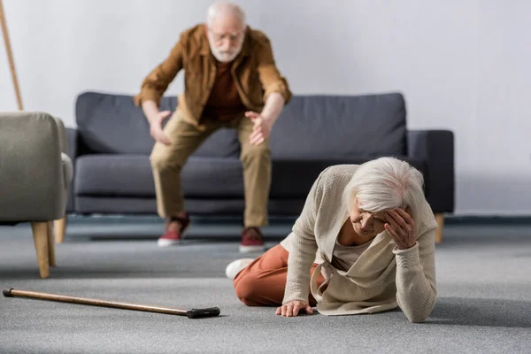 Вибірковий фокус старшого чоловіка поспішає допомогти дружині лежати на підлозі біля ходьби палиці — стокове фото