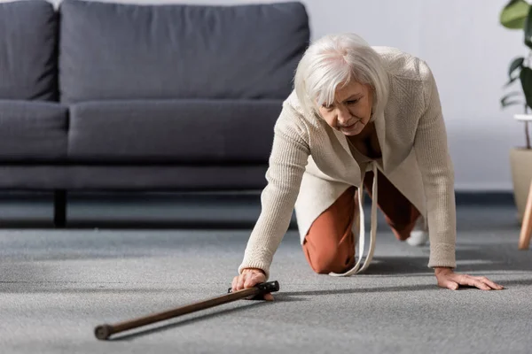 Fallen, helpless senior woman trying to get walking stick on floor — Stock Photo