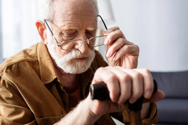 Homem sênior colocando óculos, enquanto sentado com bengala — Stock Photo