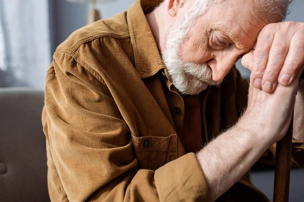 Senior, depressed man sitting with bowed head while leaning on walking stick — Stock Photo