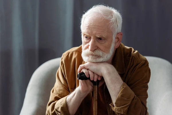 Anciano, hombre solitario mirando hacia otro lado mientras está sentado con bastón - foto de stock