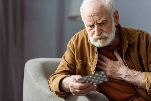 Uomo anziano sentirsi male, toccando petto e tenendo pillole — Foto stock