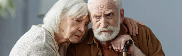 Imagen horizontal de la mujer mayor con los ojos cerrados abrazando marido, enfermo de demencia - foto de stock