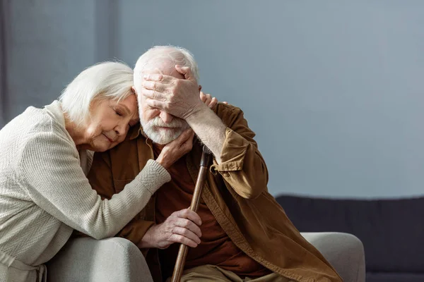 Senior man, sick on dementia, covering eyes with hand while wife embracing him with closed eyes — Stock Photo