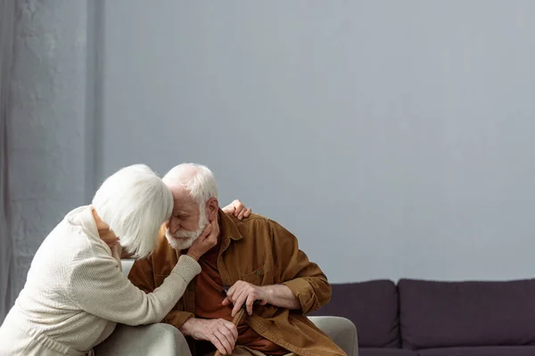 Пожилая женщина трогает лицо и обнимает мужа, больного слабоумием — стоковое фото