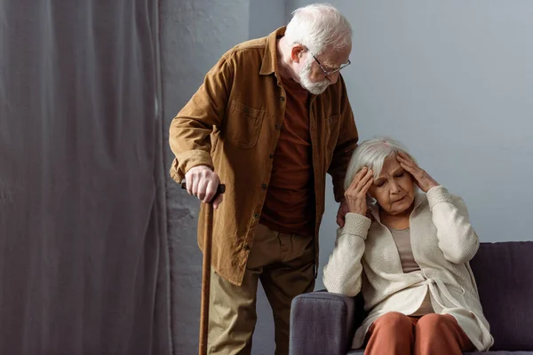 Uomo anziano con bastone da passeggio in piedi vicino moglie che soffre di hedache — Foto stock