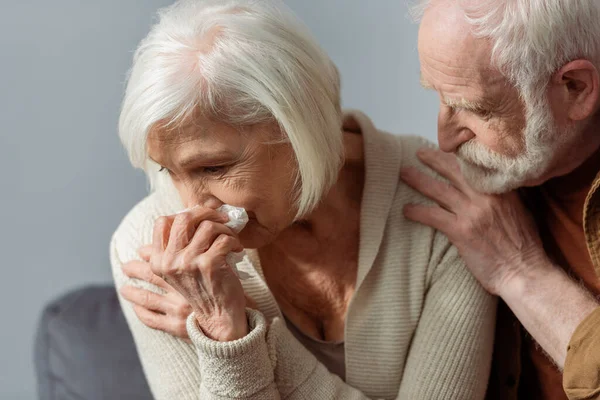 Hombre mayor tocando hombro de esposa llorando sosteniendo servilleta de papel - foto de stock