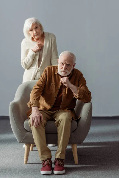 Verärgerte Seniorin berührt Brust, während sie hinter Ehemann steht, an Demenz erkrankt — Stockfoto