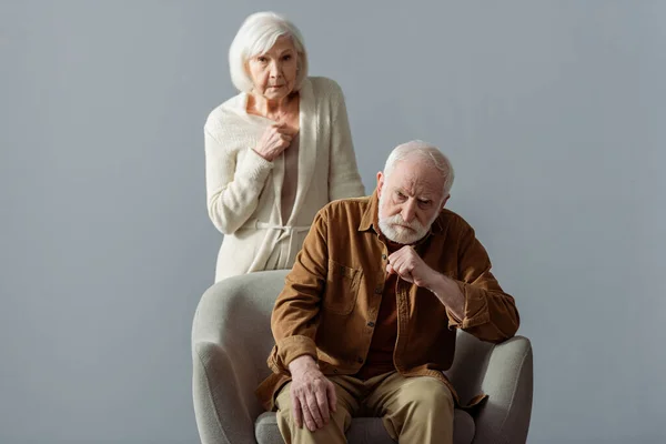 Depressed senior woman touching chest while standing behind husband, sick on dementia — Stock Photo