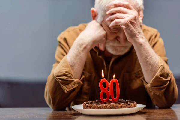 Depressed, lonely senior sitting near birthday cake with number eighty — Stock Photo