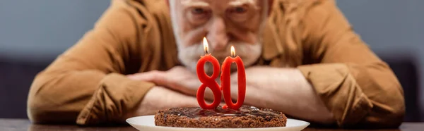 Selective focus of lonely senior man looking at birthday cake with number eighty, horizontal image — Stock Photo