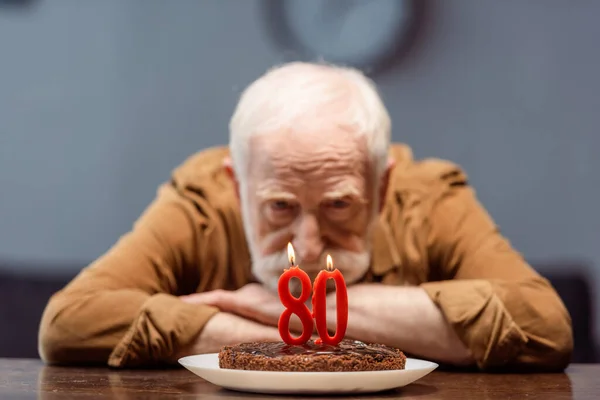 Selective focus of lonely senior man looking at birthday cake with number eighty — Stock Photo