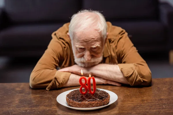 Самотній старший чоловік дивиться на торт на день народження з номером вісімдесят — стокове фото