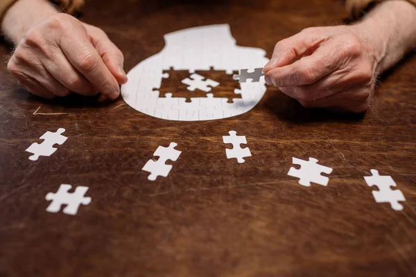 Cropped view of ill senior man collecting jigsaw puzzle for dementia therapy — Stock Photo