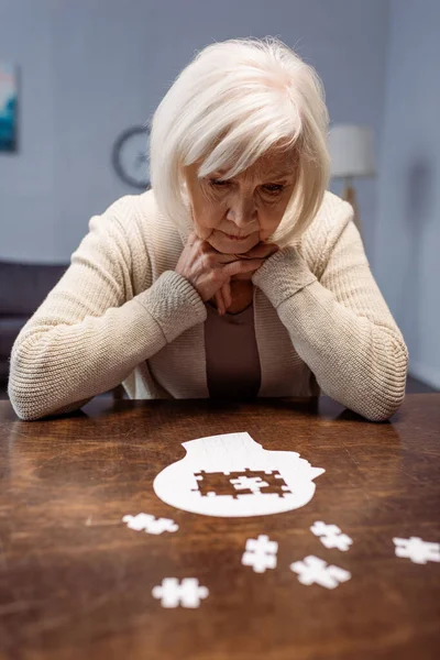 Sick senior woman thinking while collecting jigsaw puzzle as dementia therapy — Stock Photo