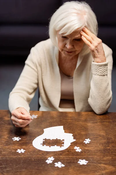 Mujer mayor tocando la cabeza mientras juega puzzle como rehabilitación de demencia - foto de stock