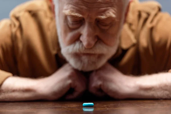 Selective focus of old man looking at pill on table — Stock Photo