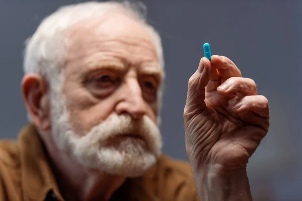 Selective focus of sad senior man holding pill — Stock Photo