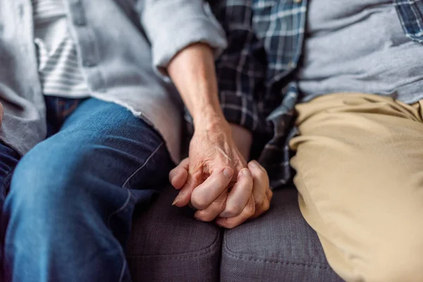 Vista recortada de la pareja de ancianos sentados en el sofá y cogidos de la mano - foto de stock