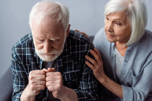 Worried senior woman touching husband suffering from dementia and sitting with clenched fists — Stock Photo