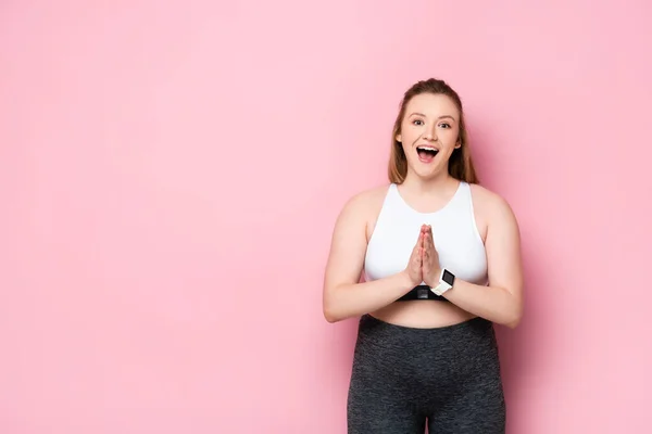 Excited overweight girl standing with praying hands on pink — Stock Photo