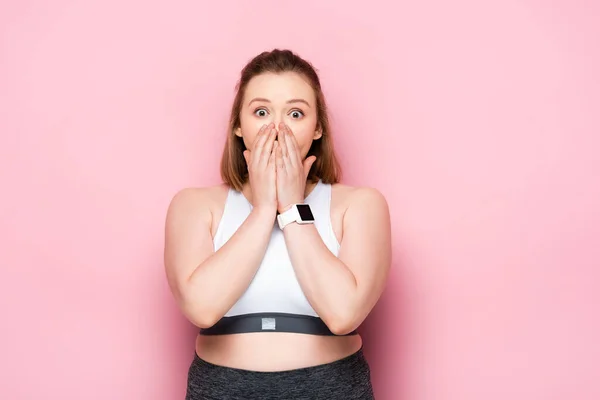 Chocado menina com sobrepeso cobrindo a boca com as mãos em rosa — Fotografia de Stock