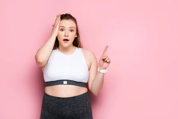 Choqué fille en surpoids touchant la tête et pointant du doigt sur rose — Photo de stock