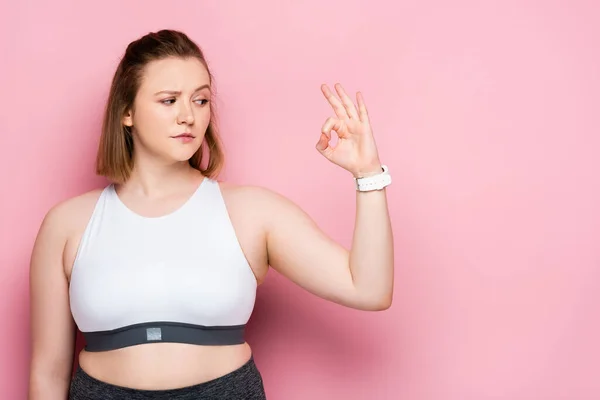 Skeptical overweight girl showing okay gesture on pink — Stock Photo