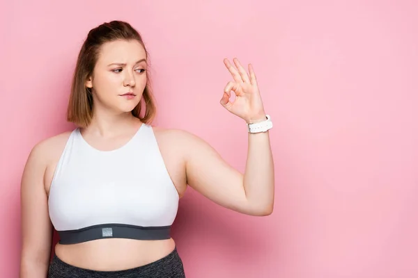 Menina com sobrepeso cético mostrando gesto ok em rosa — Fotografia de Stock