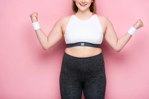 Cropped view of smiling overweight girl showing winner gesture on pink — Stock Photo