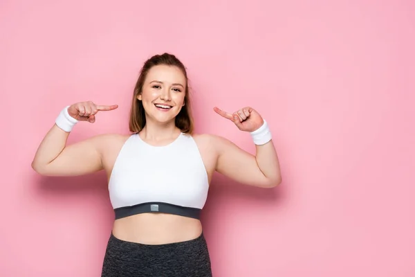 Happy overweight girl pointing with fingers at herself on pink — Stock Photo