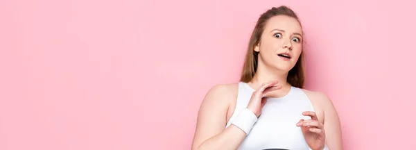 Horizontales Bild eines verängstigten übergewichtigen Mädchens, das gestikuliert, während es in die Kamera auf rosa schaut — Stockfoto