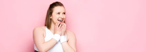 Récolte panoramique de fille en surpoids excité toucher le menton et détourner les yeux sur rose — Photo de stock