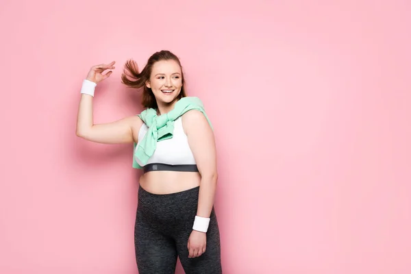 Glückliches übergewichtiges Mädchen mit Sweatshirt über den Schultern, das wegschaut auf rosa — Stockfoto