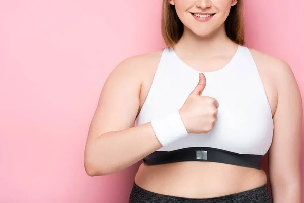 Vista ritagliata di sorridente ragazza in sovrappeso mostrando pollice su rosa — Foto stock