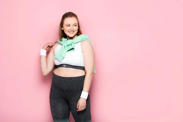 Glückliches übergewichtiges Mädchen mit Sweatshirt über den Schultern, das wegschaut auf rosa — Stockfoto