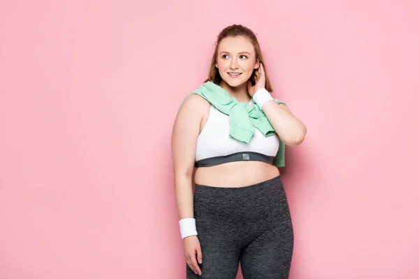 Schöne übergewichtige Mädchen mit Sweatshirt über den Schultern berührt Haare und schaut weg auf rosa — Stockfoto