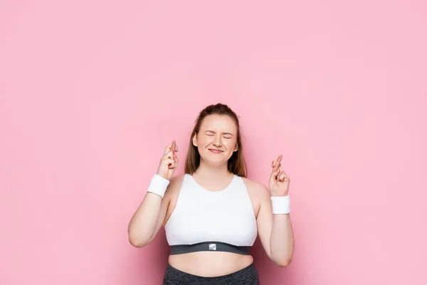 Fille en surpoids avec les yeux fermés tenant les doigts croisés sur rose — Photo de stock